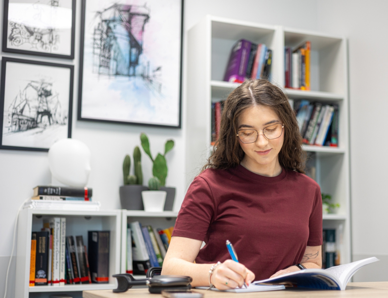 Master of Business Administration | Studia MBA w Opolu | Uniwersytet WSB Merito Opole: Uczestniczka studiów podyplomowych siedzi przy stoliku i czyta książkę