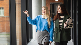 Green Leader | Studia I stopnia w Poznaniu | Uniwersytet WSB Merito w Poznaniu: Dwie studentki, kolorowo ubrane spacerują po korytarzu uczelni WSB Merito w Poznaniu 