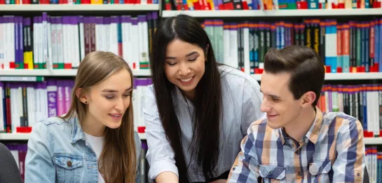 Studia II stopnia z podyplomowymi w Poznaniu | Uniwersytet WSB Merito w Poznaniu: Troje studentów wspólnie pracuje nad materiałami w bibliotece,