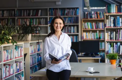 Poradniki - dzielimy się wiedzą | Uniwersytet WSB Merito: Uczestniczka MBA pozuje z informatorem w bibliotece- Uniwersytet WSB Merito Toruń