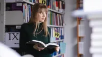 Rachunkowość od podstaw | Studia podyplomowe w Szczecinie | Uniwersytet WSB Merito Szczecin: Studentka Uniwersytetu WSB Merito spogląda za okno, przeglądając książkę w bibliotece.
