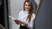 Neurologopedia | Studia podyplomowe w Szczecinie | Uniwersytet WSB Merito Szczecin: Studentka Uniwersytetu WSB Merito z uśmiechem przegląda książkę.