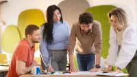 Content marketing – tworzenie treści marketingowych | Studia I stopnia w Szczecinie | Uniwersytet WSB Merito Szczecin: Grupa studentów pracuje nad projektem przy stole, analizując notatki i szkice.