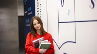 Zarządzanie w podmiotach leczniczych | Studia podyplomowe w Szczecinie | Uniwersytet WSB Merito Szczecin: Studentka z książkami przy bibliotece, gotowa do nauki
