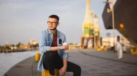 Psychologia w zarządzaniu | Studia II stopnia w Szczecinie | Uniwersytet WSB Merito Szczecin: Student WSB Merito siedzi na nadbrzeżu, w tle żurawie stoczni