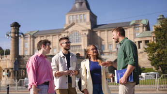 Finanse publiczne i podatki | Studia II stopnia w Szczecinie | Uniwersytet WSB Merito Szczecin: Czworo studentów rozmawia na tle gmachu Wałów Chrobrego w słoneczny dzień.