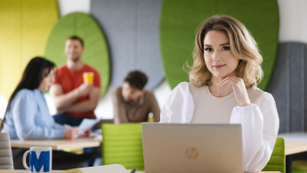 Psychologia rozwoju osobistego | Studia I stopnia w Szczecinie | Uniwersytet WSB Merito Szczecin: Studentka pracuje przy laptopie w nowoczesnej strefie wspólnej, w tle inni studenci.