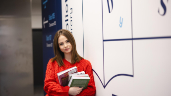 Zarządzanie w podmiotach leczniczych | Studia podyplomowe w Szczecinie | Uniwersytet WSB Merito Szczecin: Studentka z książkami przy bibliotece, gotowa do nauki
