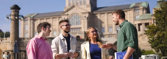 Szkolenia i kursy w Szczecinie | Uniwersytet WSB Merito Szczecin: Czworo studentów rozmawia na tle gmachu Wałów Chrobrego w słoneczny dzień.