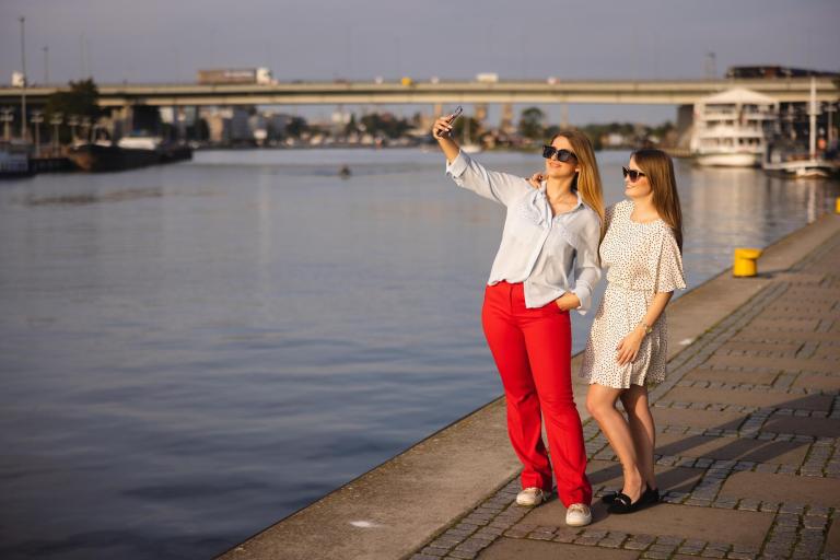 Studia jednolite magisterskie w Szczecinie | Uniwersytet WSB Merito Szczecin: Dwie studentki Uniwersytetu WSB Merito Szczecin robią selfie nad Odrą w słoneczny dzień.