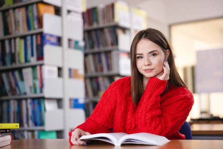Szkoły | Uniwersytet WSB Merito Szczecin: Studentka Uniwersytetu WSB Merito czyta książkę w bibliotece.