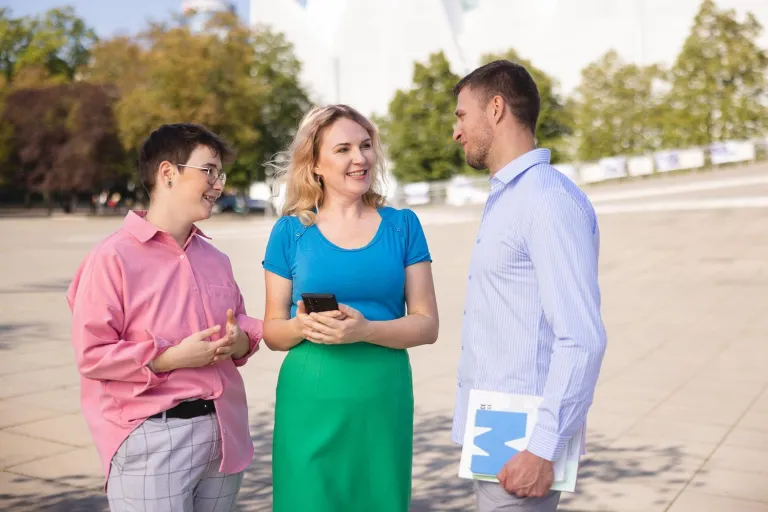 Bezpieczeństwo w biznesie i administracji | Studia I stopnia w Szczecinie | Uniwersytet WSB Merito Szczecin: Trzy osoby rozmawiają na placu przed nowoczesnym budynkiem.