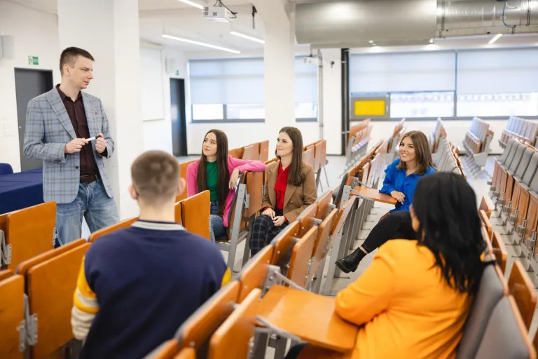 Wyniki wyszukiwania | Uniwersytet WSB Merito Szczecin: Wykładowca rozmawia ze studentami w auli, prowadząc swobodne zajęcia w małej grupie.