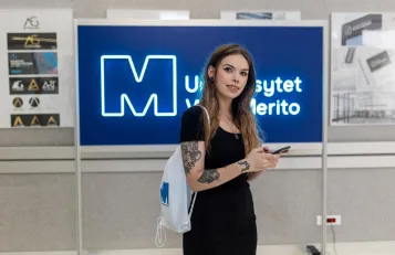Nasze wartości | Uniwersytet WSB Merito w Toruniu: studentka z telefonem w ręku na korytarzu uniwersytetu