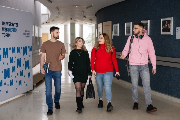 Samorząd studencki | Uniwersytet WSB Merito w Toruniu: Grupa czterech studentów idzie korytarzem uniwersytetu WSB Merito w Toruniu