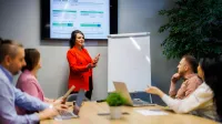 Kadry i płace | Studia podyplomowe w Warszawie | Uniwersytet WSB Merito Warszawa: kobieta omawiająca projekt wśród grupy ludzi