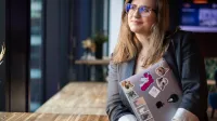 MBA HR | Studia MBA w Warszawie | Uniwersytet WSB Merito Warszawa: Uczestniczka studiów MBA pozuje z laptopem na korytarzu- Uniwersytet WSB Merito w Warszawie