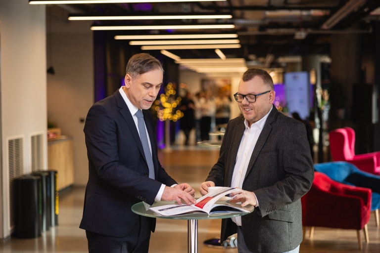 Zasady rekrutacji | Uniwersytet WSB Merito Warszawa: Uczestnicy studiów MBA stoją przy stoliku- Uniwersytet WSB Merito w Warszawie